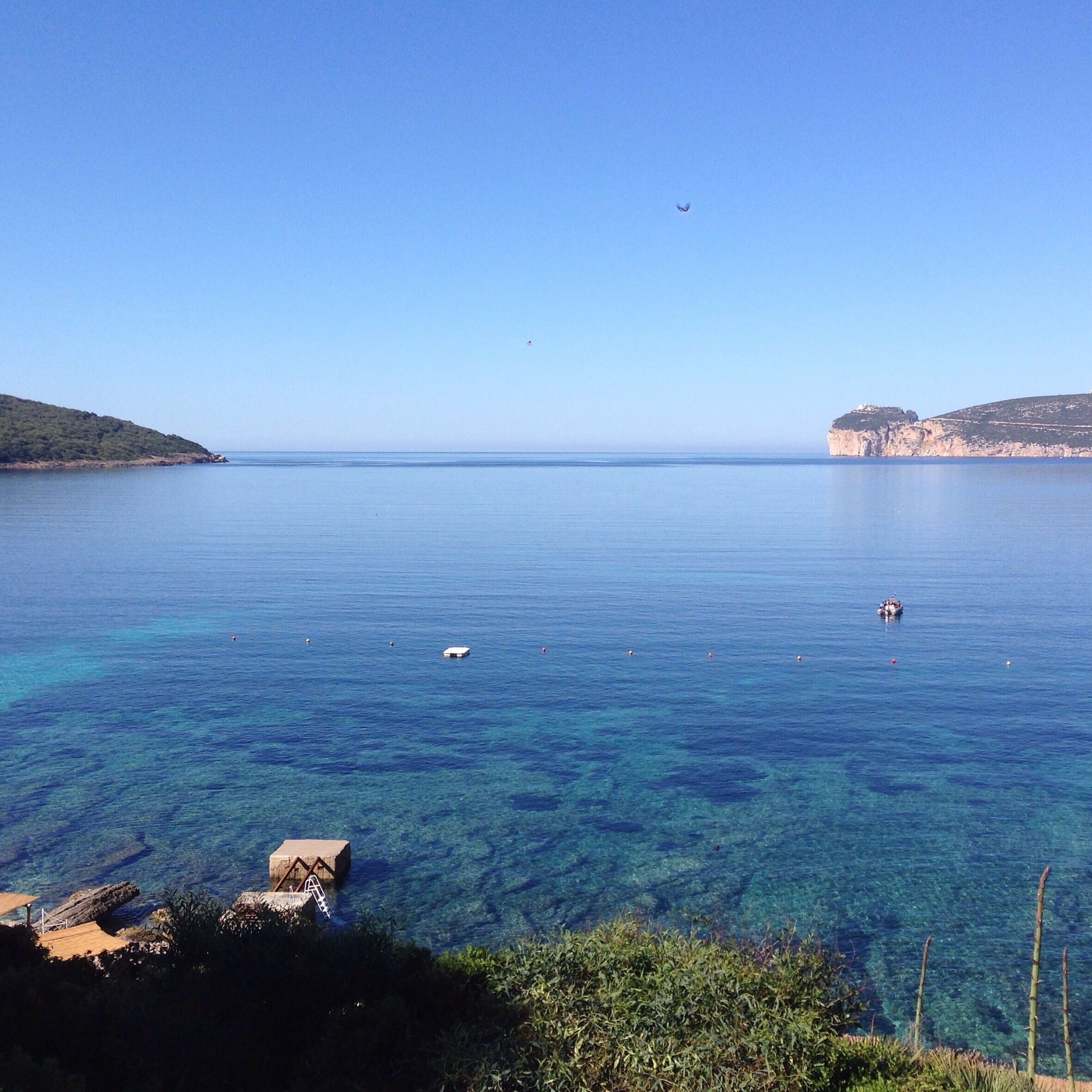 A clear blue sea with a rocky coastline and cliffs in the distance.