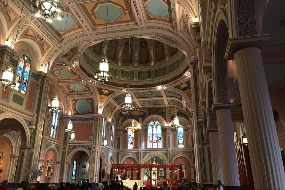Interior de igreja ornamentado com altos tetos, vitrais e altar central.