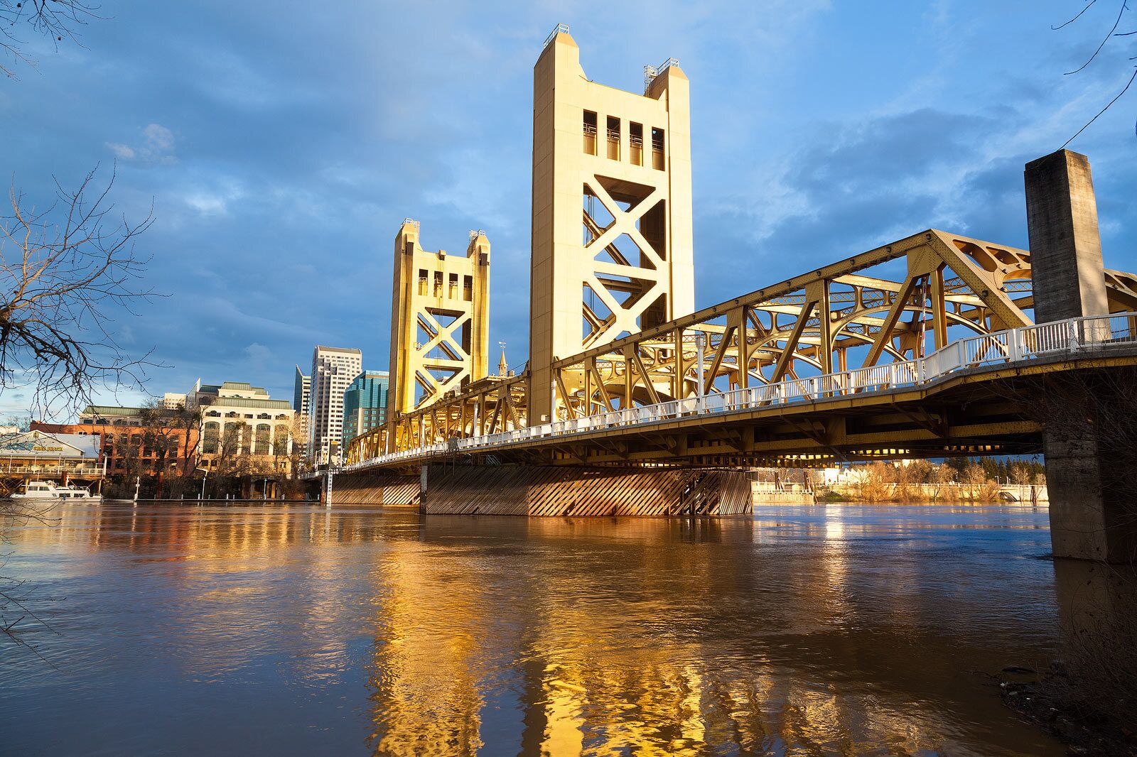 Un puente con una estructura de celosía única que cruza un río, con edificios al fondo.