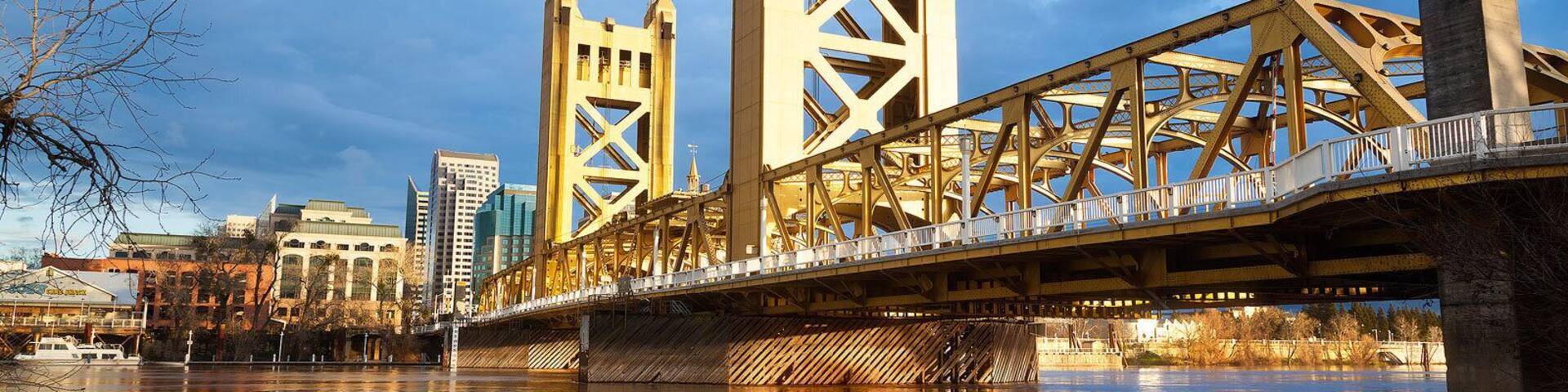 A bridge with a unique lattice structure spanning a river, with buildings in the background.