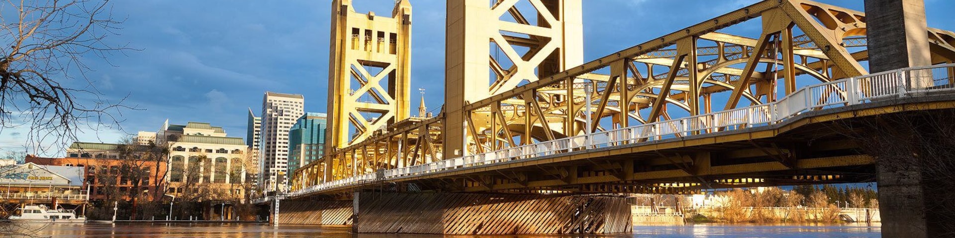 Un puente con una estructura de celosía única que cruza un río, con edificios al fondo.