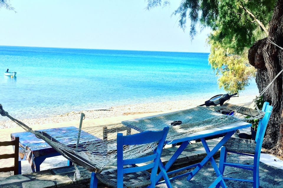 A beach with blue chairs and a hammock overlooking the sea.
