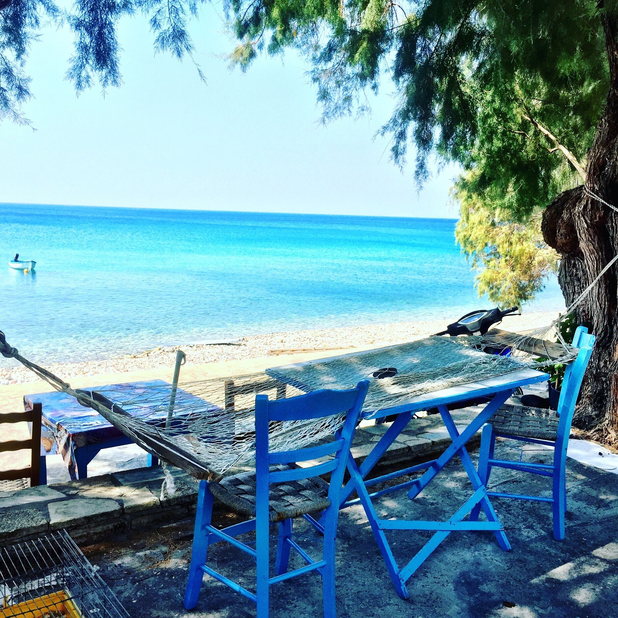 A beach with blue chairs and a hammock overlooking the sea.