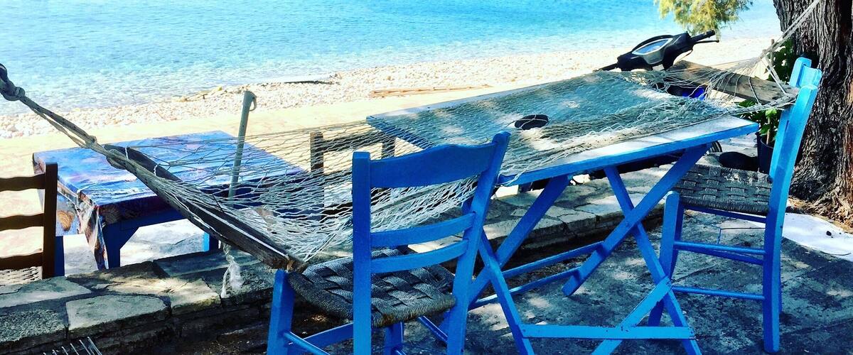 A beach with blue chairs and a hammock overlooking the sea.