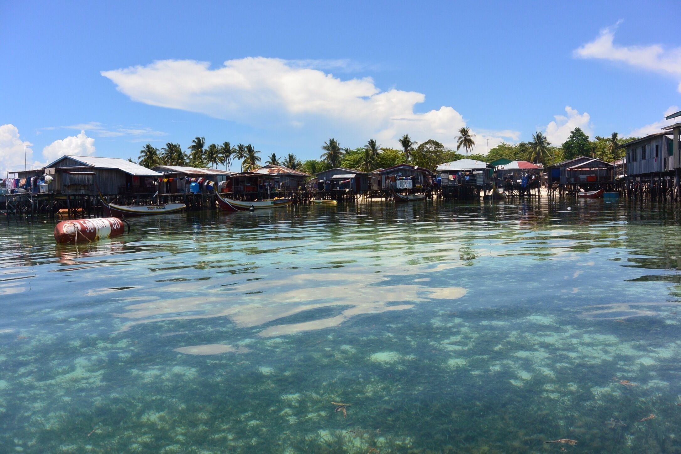A clear water body with houses on stilts and boats.