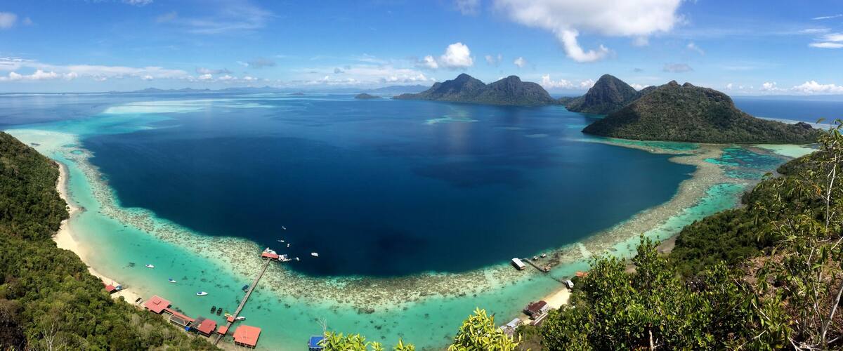 A coastal landscape with clear turquoise waters, a sandy beach, and lush green hills.