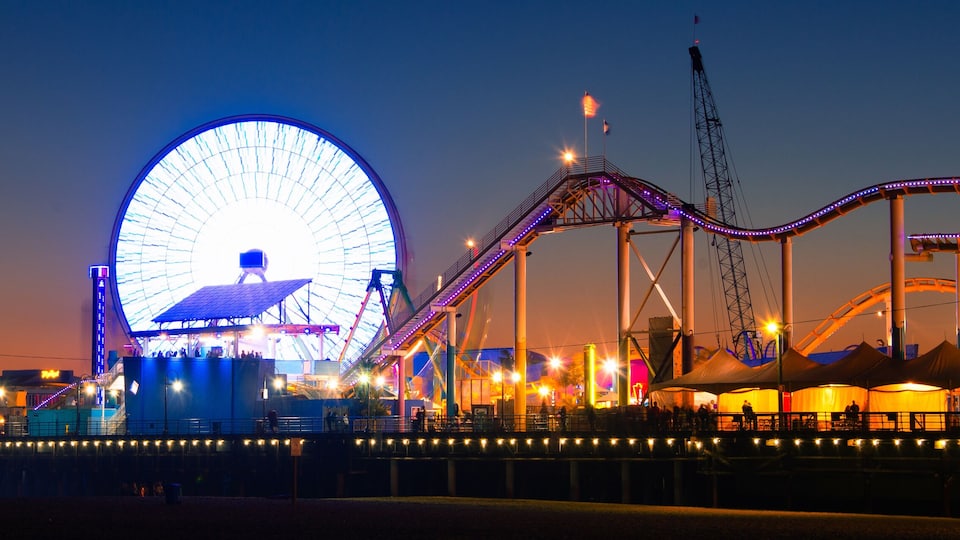 A Ferris wheel and a roller coaster at an amusement park at dusk.