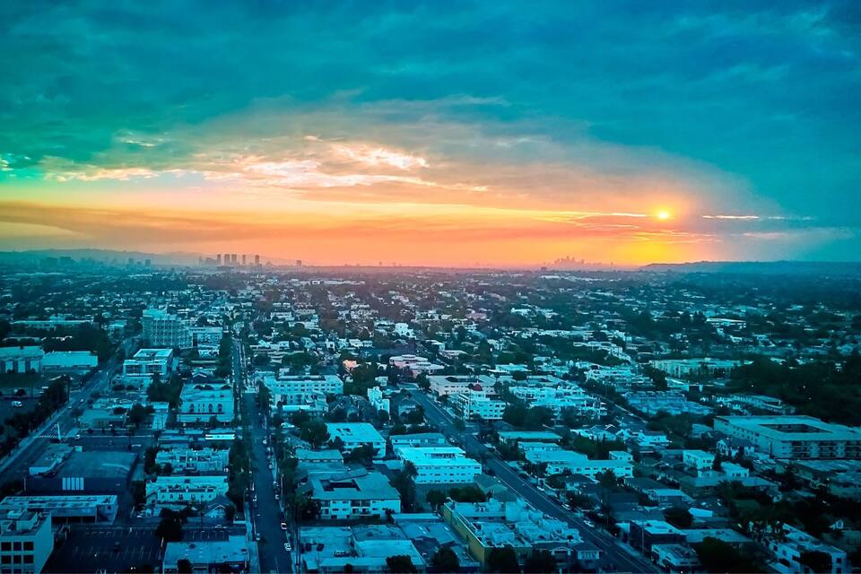 Paisagem urbana ao pôr do sol, com céu claro e sol visível próximo ao horizonte.