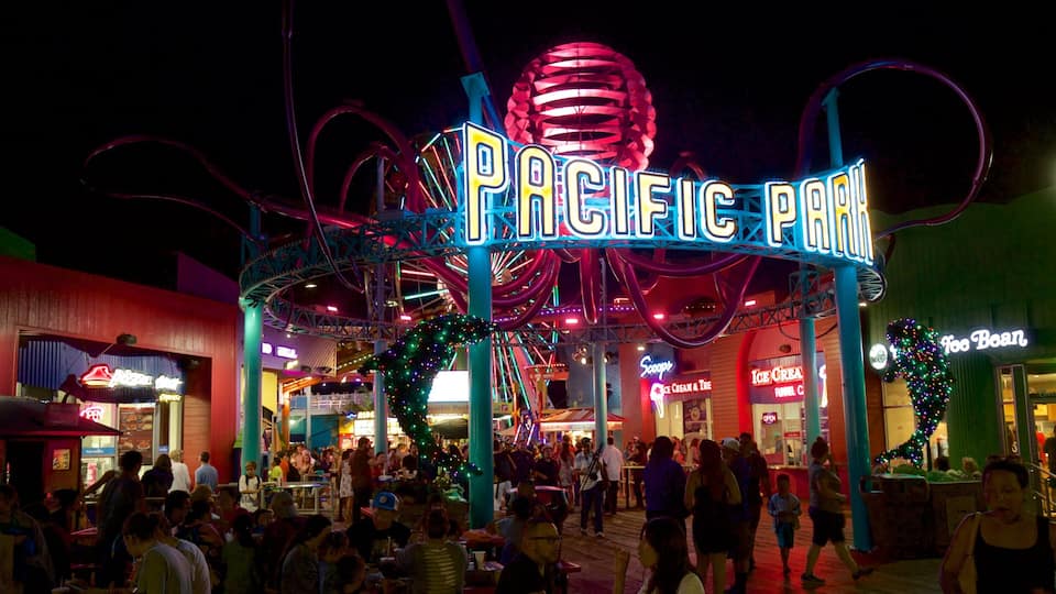 A brightly lit amusement park with a neon sign reading "PACIFIC PARK" and various shops and attractions.