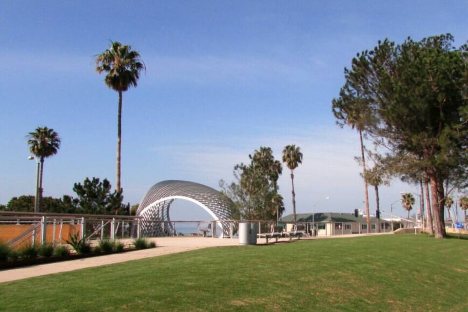 A modern architectural structure with a curved roof, surrounded by palm trees and a grassy area.