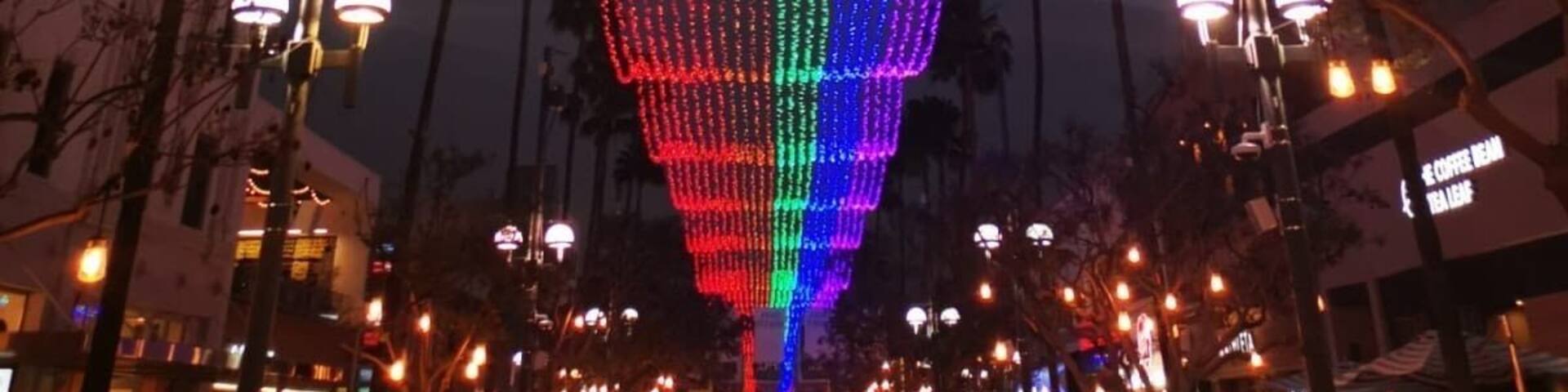 A large, illuminated structure with a rainbow color pattern, surrounded by palm trees and street lamps.