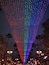 Una estructura grande e iluminada con un patrón de colores de arcoíris, rodeada de palmeras y farolas.