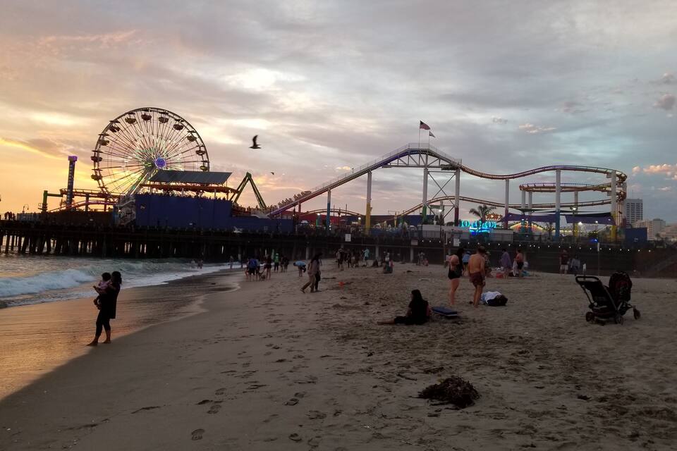 A beach with a roller coaster and a Ferris wheel in the background.
