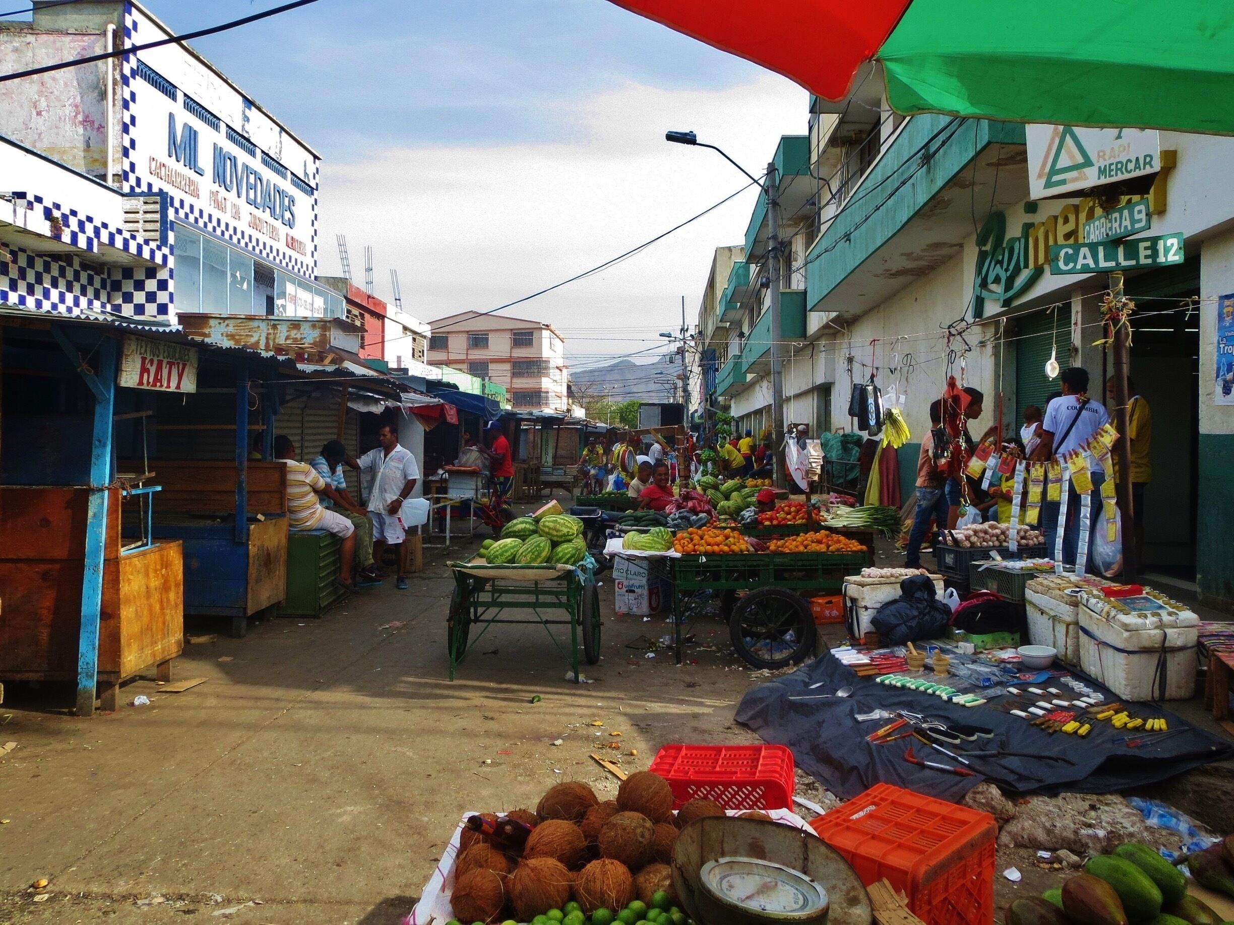 A bustling street market with vendors selling fruits, vegetables, and coconuts.