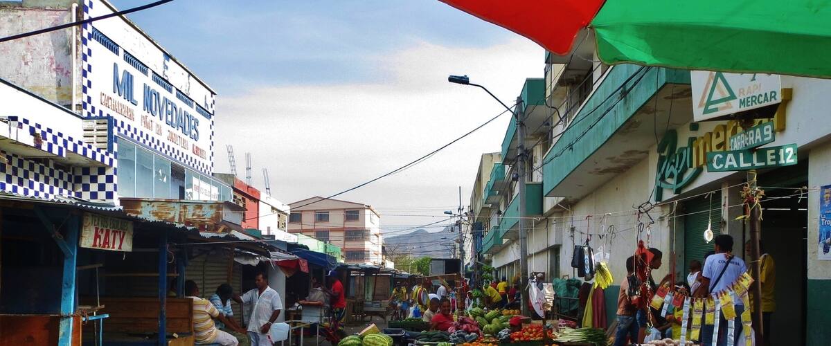 A bustling street market with vendors selling fruits, vegetables, and coconuts.