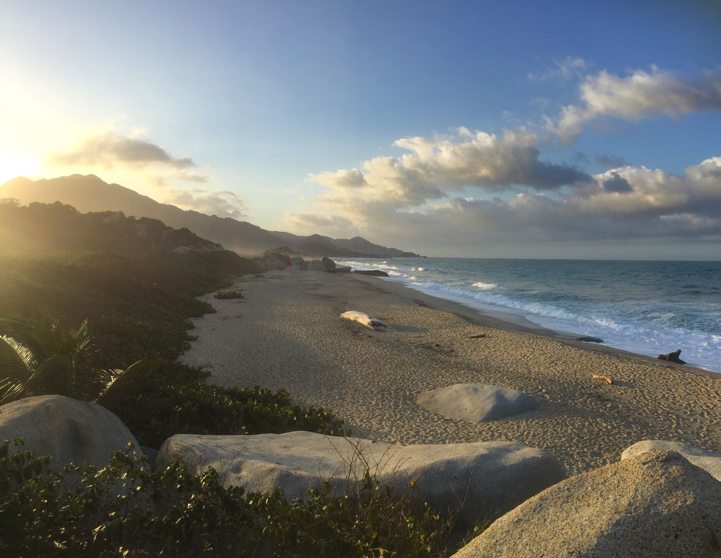 Une plage avec de gros rochers, des vagues et une montagne en arrière-plan.