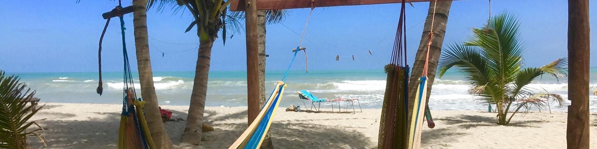 A hammock hanging between palm trees on a sandy beach with the ocean in the background.