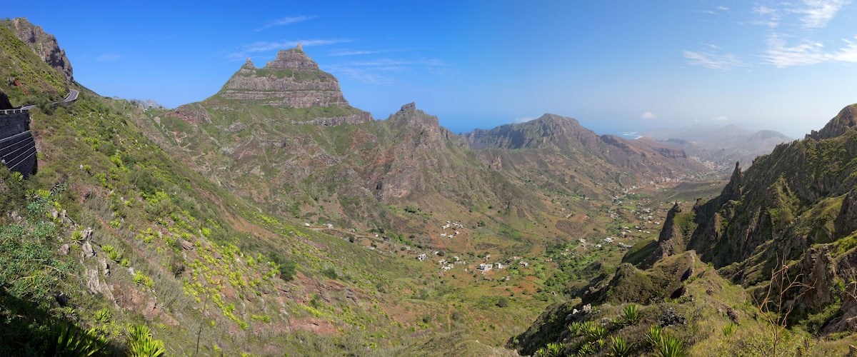 A mountainous landscape with a prominent peak, a winding road, and scattered houses.