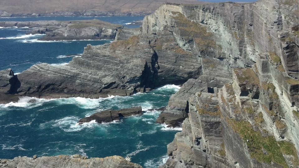 A rugged coastline with steep cliffs and turbulent sea waves crashing against the rocks.