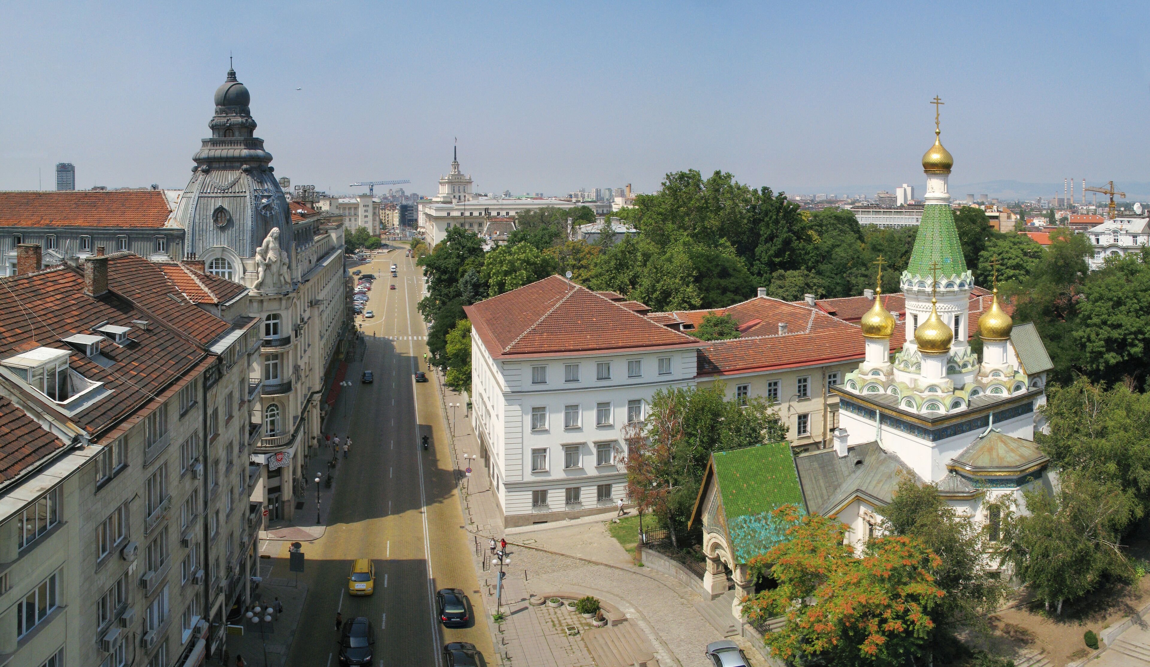 A cityscape with historic buildings, a prominent church with golden domes, and a clear blue sky.