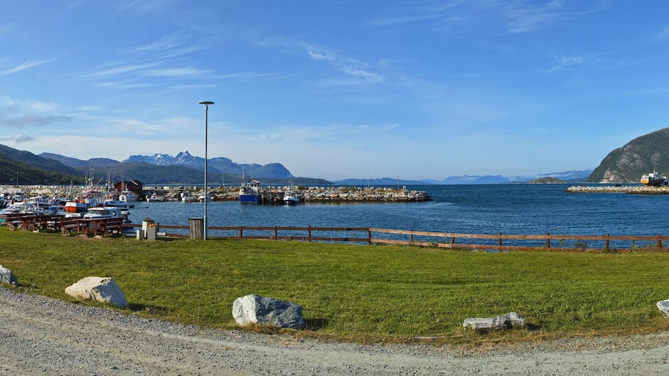 A coastal harbor with boats, a ferry, and a mountainous backdrop.