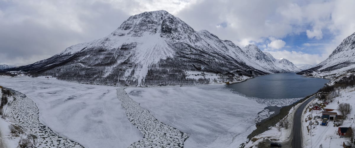 A snow-covered mountain range with a frozen lake and a road leading to a small settlement.
