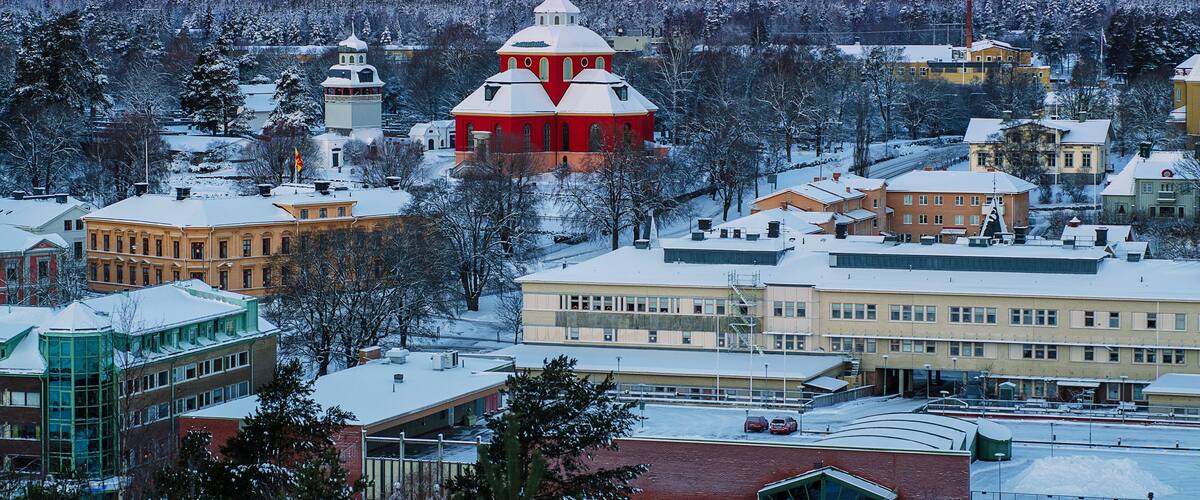 A snow-covered town with a prominent red church, a bell tower, and a mix of residential and commercial buildings.