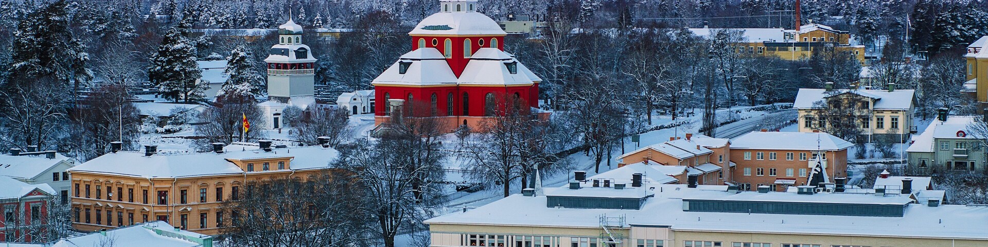 A snow-covered town with a prominent red church, a bell tower, and a mix of residential and commercial buildings.