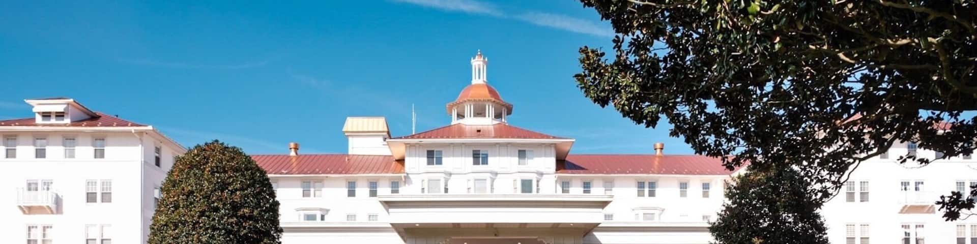 A large white building with a red roof and a dome, surrounded by well-maintained lawns and a large hedge spelling out 'PENINSULA'.