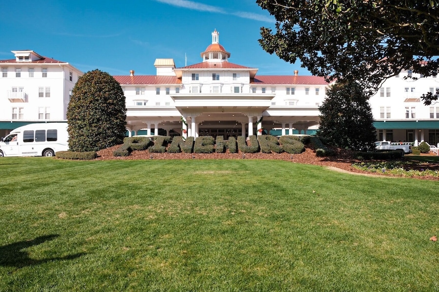 A large white building with a red roof and a dome, surrounded by well-maintained lawns and a large hedge spelling out 'PENINSULA'.