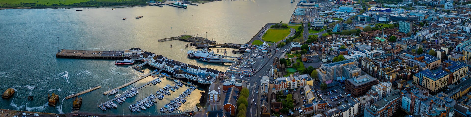 An aerial view of a harbor with boats, a large ship, and a cityscape with buildings and a river.