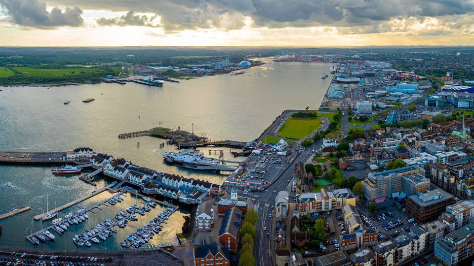 An aerial view of a harbor with boats, a large ship, and a cityscape with buildings and a river.