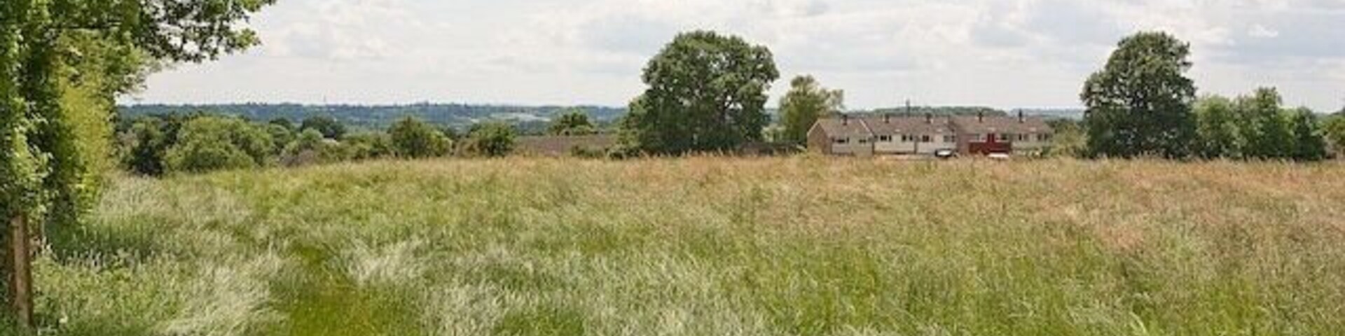 Un campo cubierto de hierba con un edificio a lo lejos y árboles alrededor.
