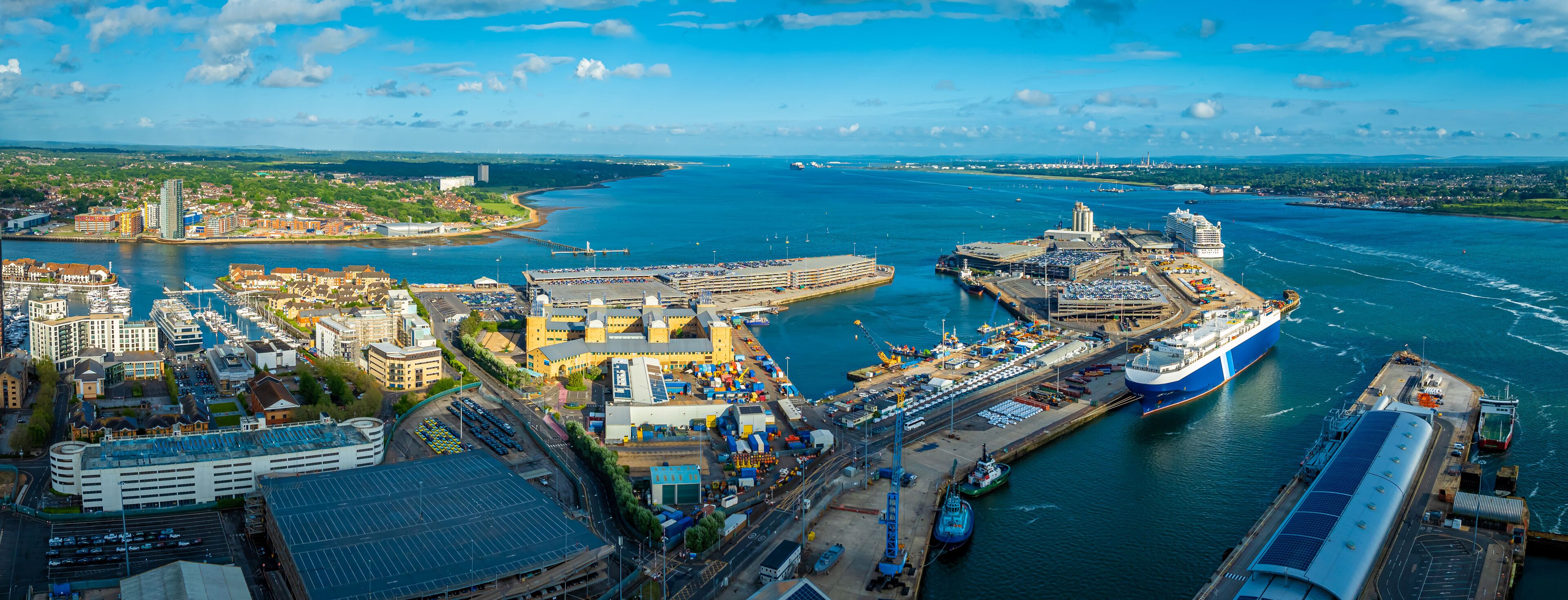 A harbor with a large cruise ship docked, a bridge, and a cityscape with buildings and greenery.