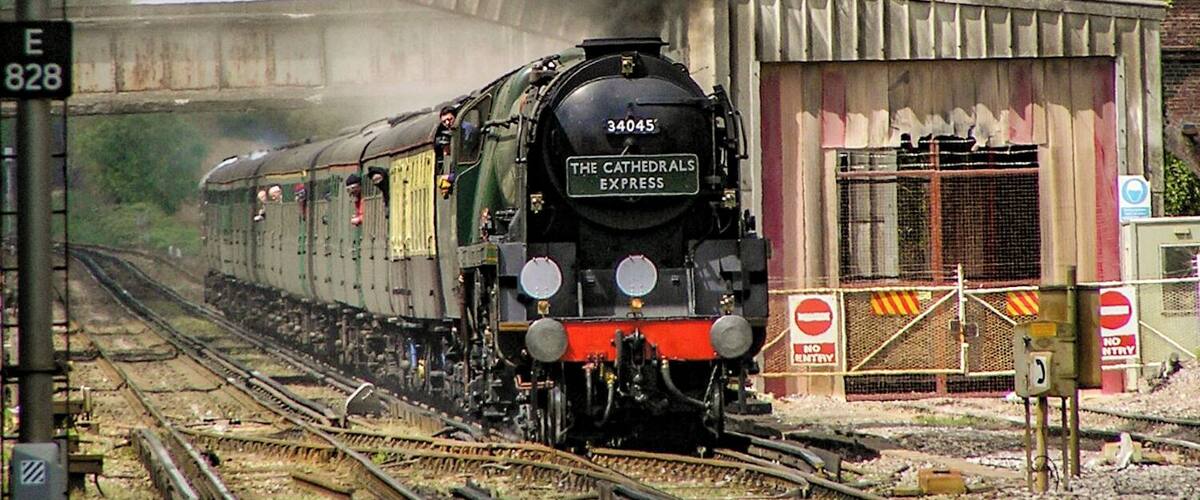 A steam locomotive with the number 34045, named 'The Cathedrals Express', emitting smoke as it travels on railway tracks.