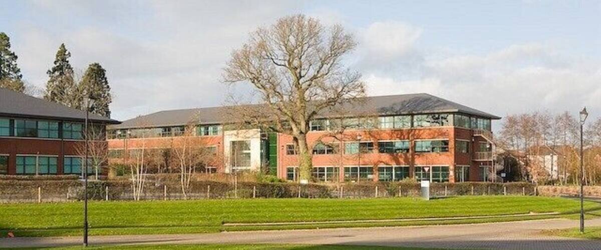 A modern building with a glass facade, surrounded by a well-maintained lawn and a fence.