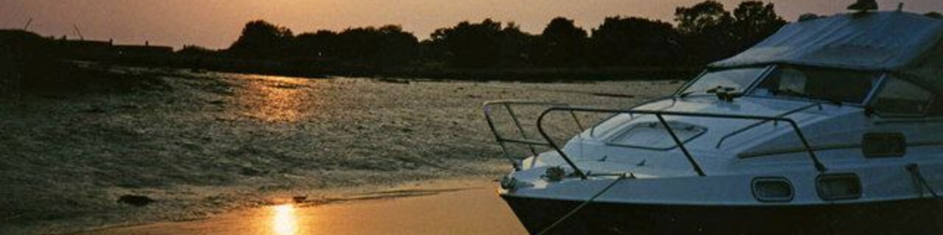 Um barco atracado ao pôr do sol, com águas calmas e um cais de madeira.