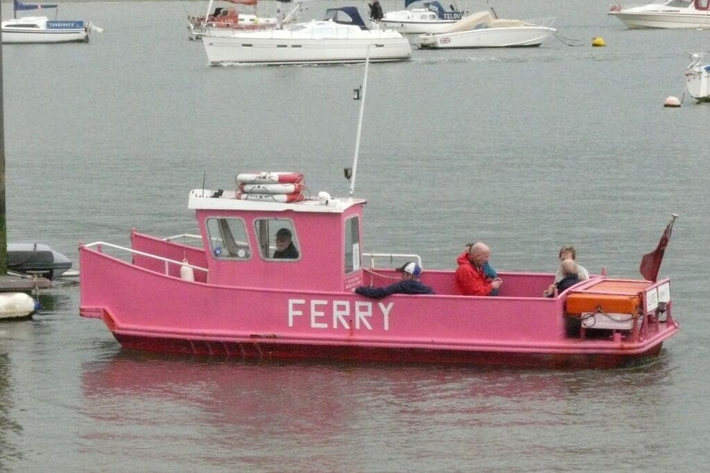 A pink ferry with the word "FERRY" on it, docked at a harbor with other boats.