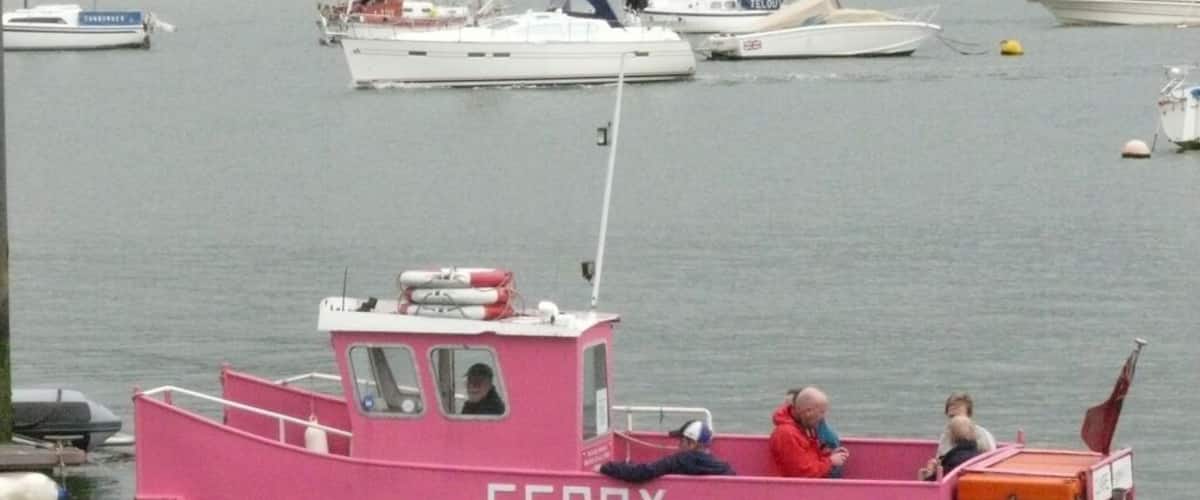 A pink ferry with the word "FERRY" on it, docked at a harbor with other boats.