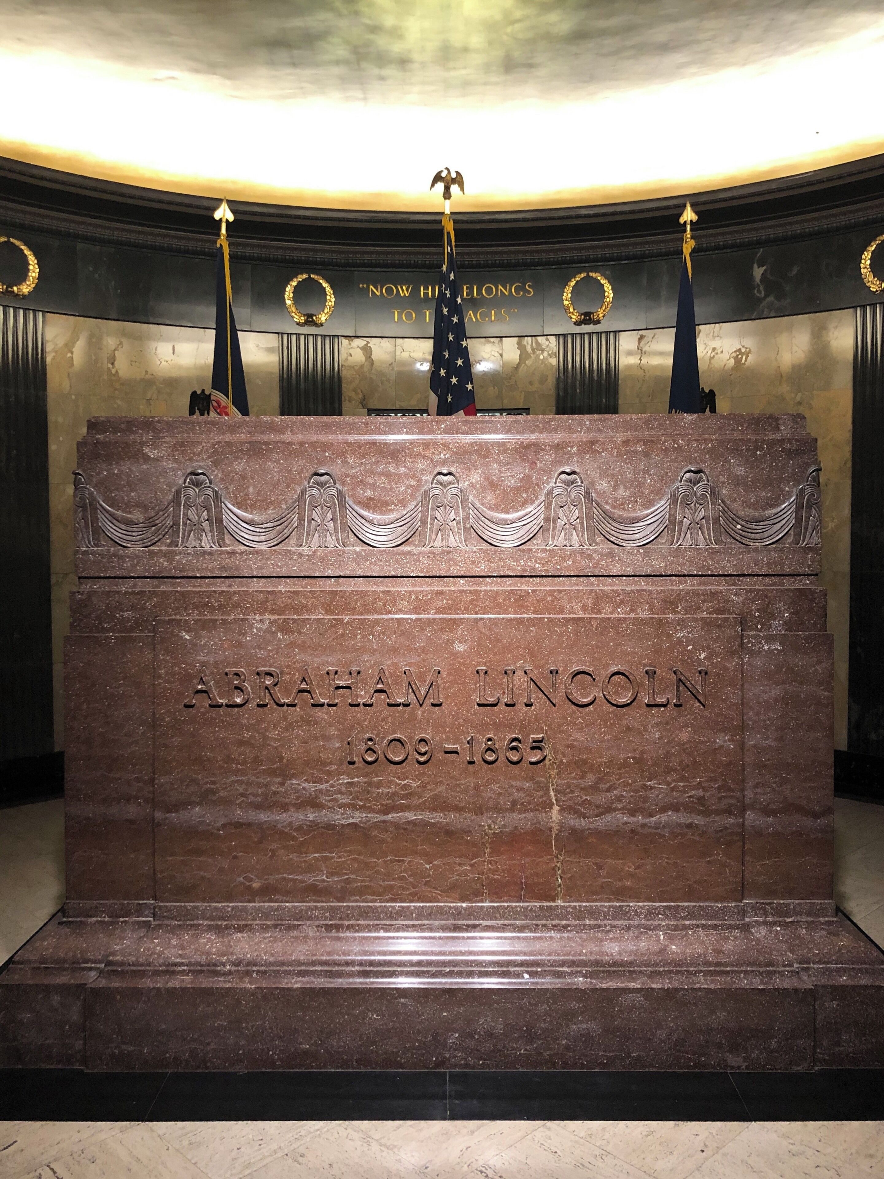 Abraham Lincoln's tomb with an eagle statue on top, surrounded by flags and a plaque with his name and dates.