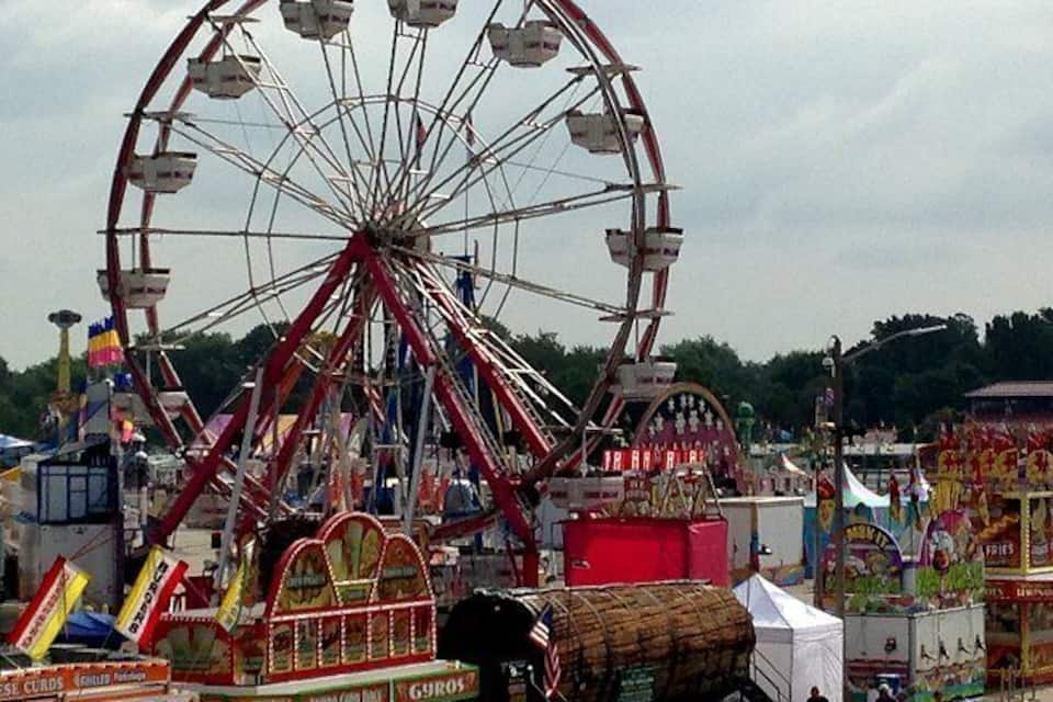 A large Ferris wheel, a carousel, and various amusement rides at a fair.