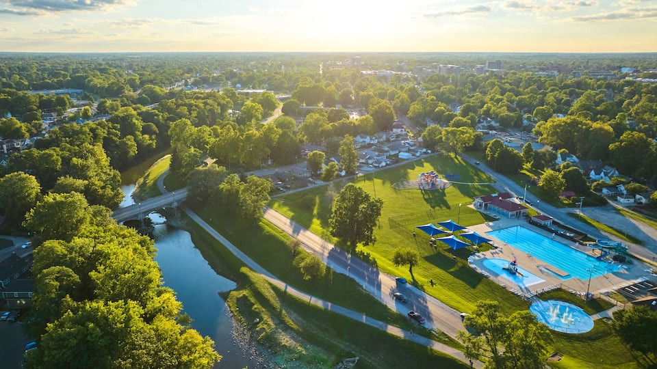 An aerial view of a park with a swimming pool, a bridge, and a river.
