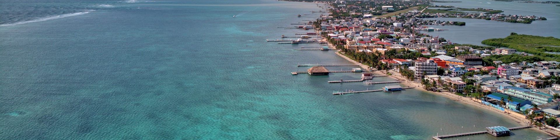 A coastal town with clear turquoise waters, a pier, and a thatched-roof structure.