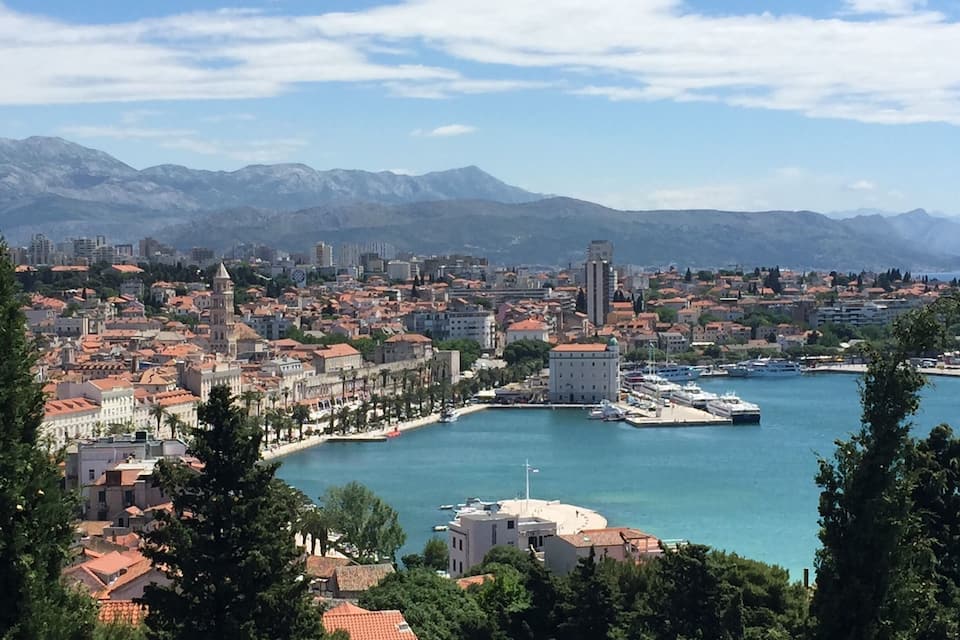 A coastal city with a harbor, historic buildings, and mountains in the background.