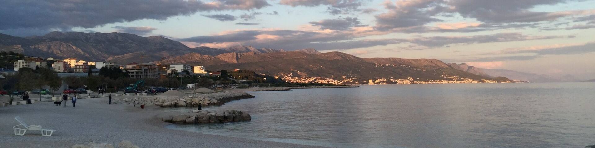 A coastal town with a pebbled beach, calm water, and mountains in the background.