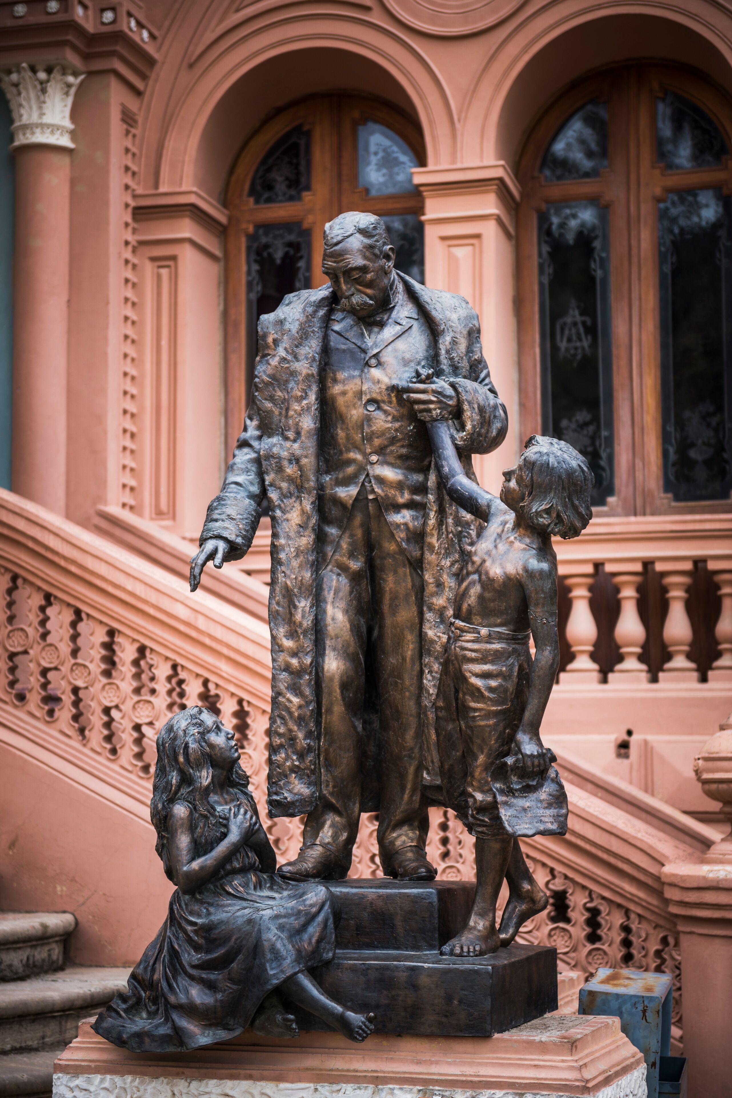 Una estatua de un hombre y un niño sobre un pedestal, con un elaborado fondo arquitectónico.
