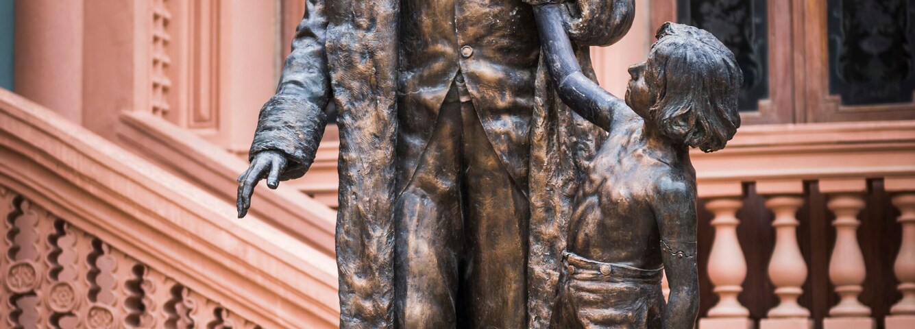 Una estatua de un hombre y un niño sobre un pedestal, con un elaborado fondo arquitectónico.