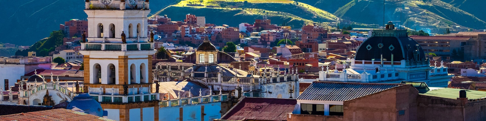 Uma cidade com uma torre do relógio imponente, um edifício em formato de cúpula e colinas ondulantes ao fundo.