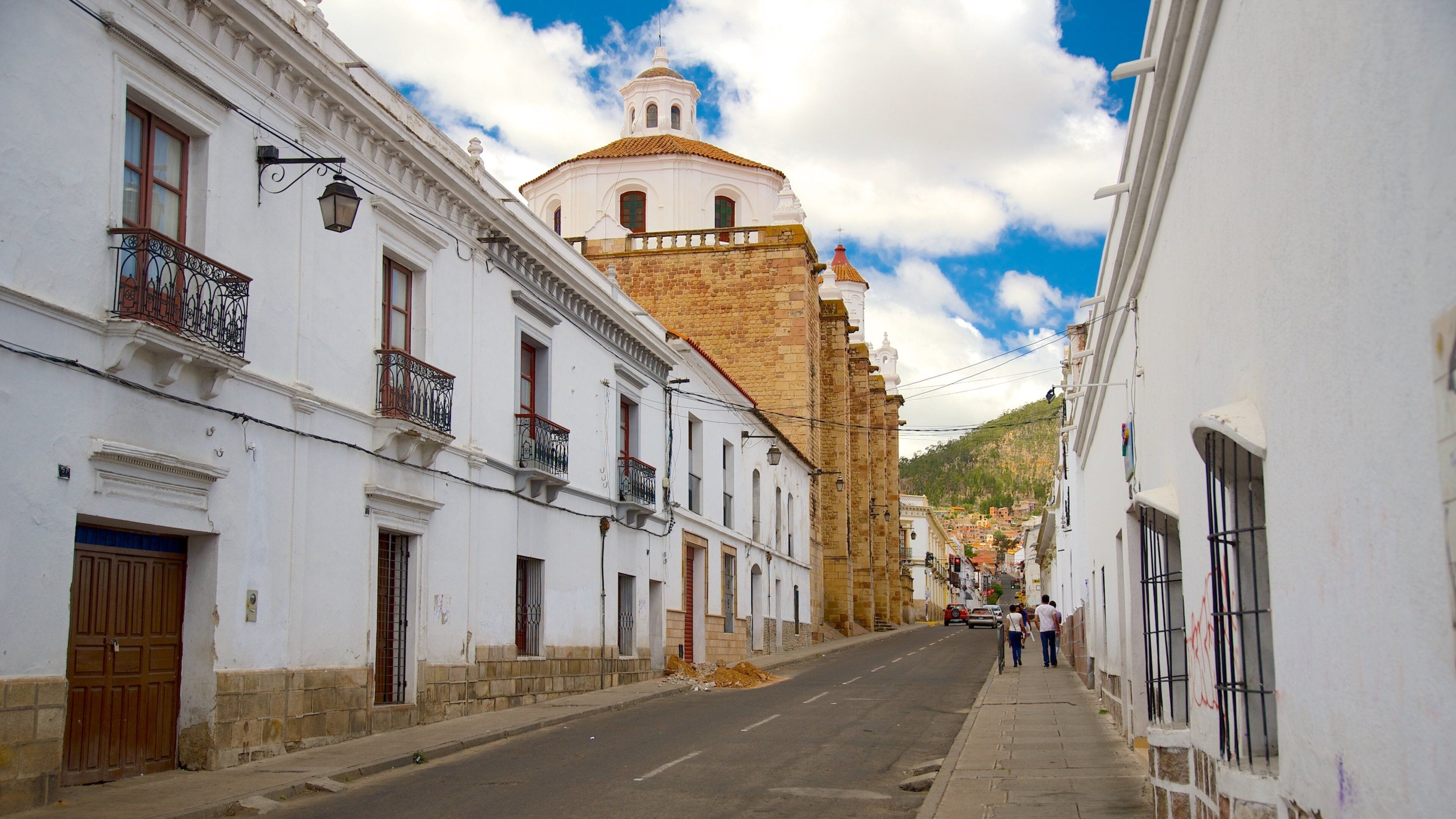 Una calle estrecha bordeada por edificios blancos con balcones y una iglesia destacada con cúpula al fondo.