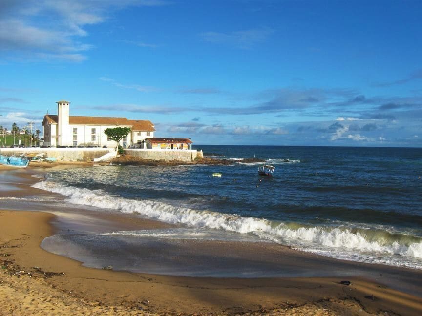 A beach with waves, a building, and a boat.